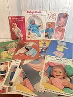 Group of vintage baby knitting/crochet pattern booklets spread on table