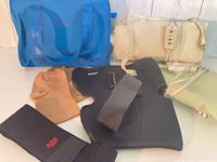Group shot of all six items: blue duffel, cream heating pad with controller, black knee brace, black ACE wrist brace, beige wrist glove, green elastic support