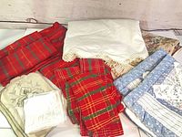 Group view showing red plaid linens, cream crochet-edge sheet, blue patchwork quilt and embroidered pieces