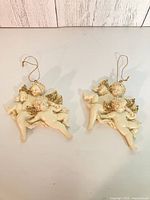 Two matching cream resin cherub angel ornaments with gold wings and hanging cords