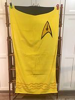 Full view of towel showing yellow body, black delta insignia, orange wave border