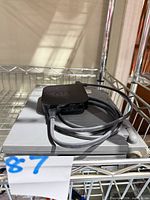 Apple TV sitting on closed PowerBook with grey cable attached