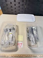 Two plastic bins containing sealed stainless steel flatware pieces