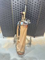 Tan canvas golf bag on metal two-wheel cart with clubs inserted
