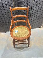 Front view of wooden chair showing curved back rails, arm supports and cane seat