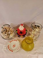 Group shot showing all five items: two glass vessels with shells, Santa figurine, yellow vase and Hasen-Bräu ashtray