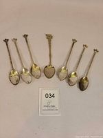 All seven silver-plated souvenir teaspoons displayed bowl-down showing ornate handles