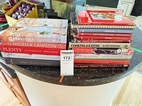 Stack of approximately 18 cookbooks on countertop