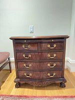 Front view showing five drawers, brass pulls, carved apron and feet
