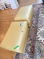 Both yellow satin ottomans side by side on hardwood floor
