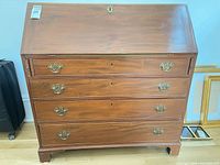 Full front view of wooden slant-front secretary desk with drawers and brass pulls