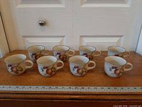 All eight mugs lined in two rows showing fruit graphics and green rims