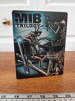 Front view of Men in Black Trilogy SteelBook showing title and alien artwork
