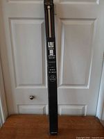 Full view of boxed Umbra curtain rod set leaning against door