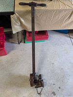 Full view of farm tool showing T-handle, long shaft, gear and chain assembly