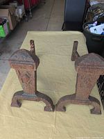 Front view of andirons showing rusted patina and decorative pattern