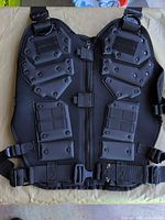 Front view of black protective vest showing armor plates, zipper, buckle and straps