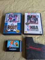 Front view of NHLPA Hockey '93 and NBA Showdown '94 clamshell boxed games, loose Sonic-labeled Genesis cartridge, black Nintendo dust sleeve