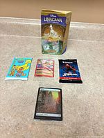 All five items laid out: Lorcana starter deck box, Sesame Street pack, foil MTG single, MTG booster pack, foil land card in sleeve