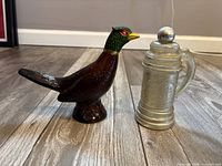 Pheasant decanter and stein bottle side by side on floor
