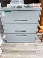 Front view of gray metal 3-drawer lateral file cabinet with lock and organizer box on top