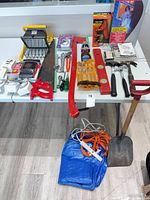 Full table view of mixed hand tools, boxed ladder and work-light