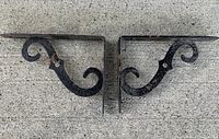 Pair of scrolled iron shelf brackets lying flat showing design and condition