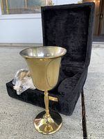 single brass goblet positioned in front of open velvet case