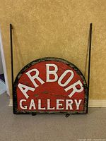 Front view of red painted wooden Arbor Gallery sign within iron frame stand