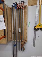 Seven metal bar clamps hanging vertically in wooden rack
