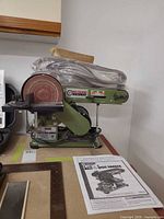 Full view of sander with sanding belts on top and manual beside