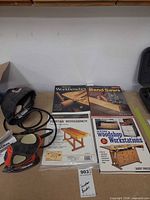 Overall lot showing sander, cord, manual, sanding pads, and four woodworking publications on table