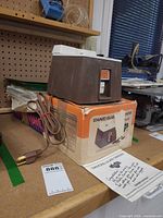 Grinder on original box with power cord and stack of stained glass sheets visible