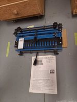Blue dovetail joint fixture with manual laid beside it on floor