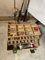 Tackle box open showing lures, hooks, bobbers, spare reel; three rods visible behind