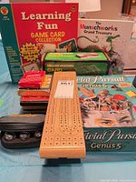 Group shot of all items including Trivial Pursuit box, Learning Fun set, book, cribbage board, card shuffler box