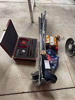 Open wooden case showing contents of putting set next to clubs, boxes and bag of balls