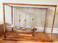 Front view of model ship within wood-framed plexiglass case