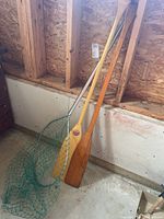 Two wooden canoe paddles and green mesh fishing net leaning against wall