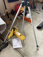 Tripod sprinkler showing aluminum legs, yellow sprinkler head, user manual