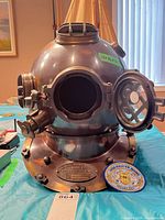 Front view of replica diving helmet with open front window and patch on table
