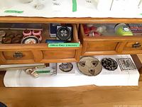 Drawer with mixed napkin rings, coasters, candles and tin, plus additional trivets and warming tray below