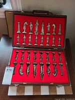Open wooden case showing complete set of metal chess pieces set in red felt insert, stone board partially visible beneath