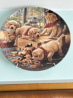 Round porcelain plate showing four golden retriever puppies playing with toys