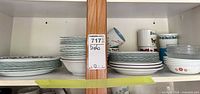 Cabinet shelves showing stacked Corelle plates, bowls, mugs in various patterns