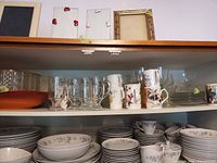 Shelf view showing porcelain mugs, pressed glass footed mugs, coloured-stem wine glasses, coupes, side plates