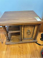 Full view of oak veneer end table showing top, cabinet door, open shelf, turned leg