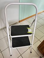 Front view of white 2-step folding stool showing both steps and handle