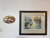 Framed deer print beside oval wooden elephant plaque displayed on wall