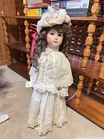 Full front view of doll with bonnet, dress, capelet, stand
